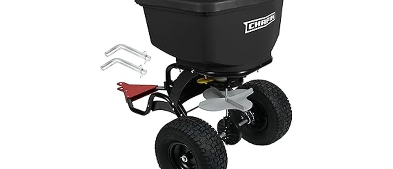 This image shows a person using a large wheeled seed spreader on a vast green lawn.